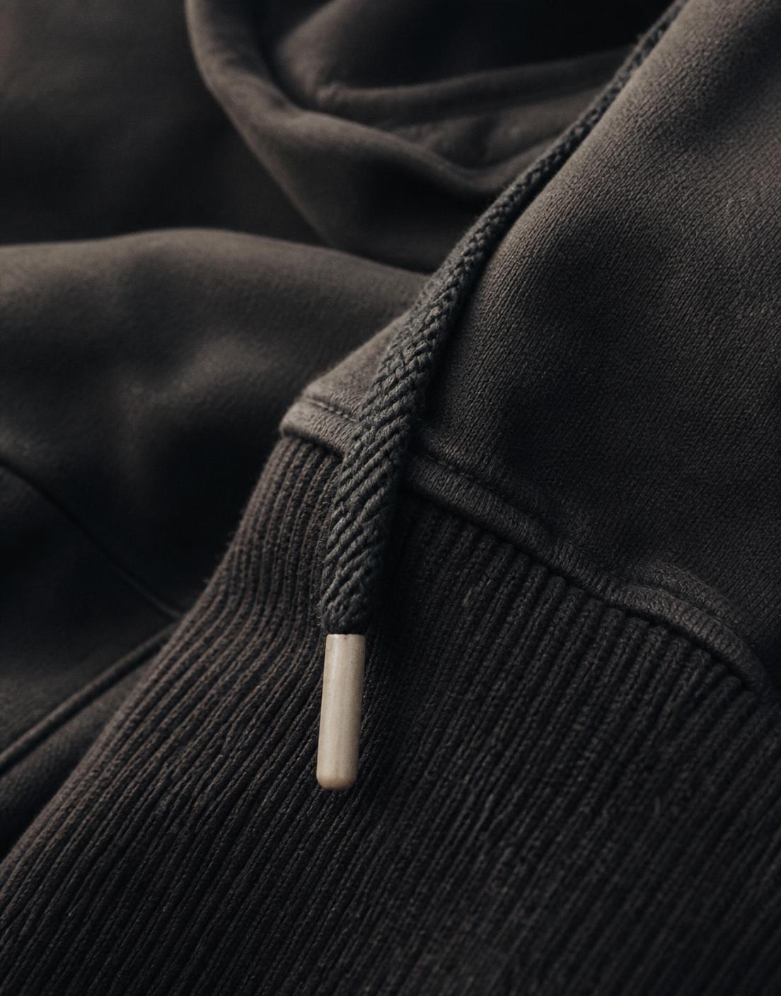 Close detail of a heavyweight black hoodie drawcord and ribbed cuff in warm light