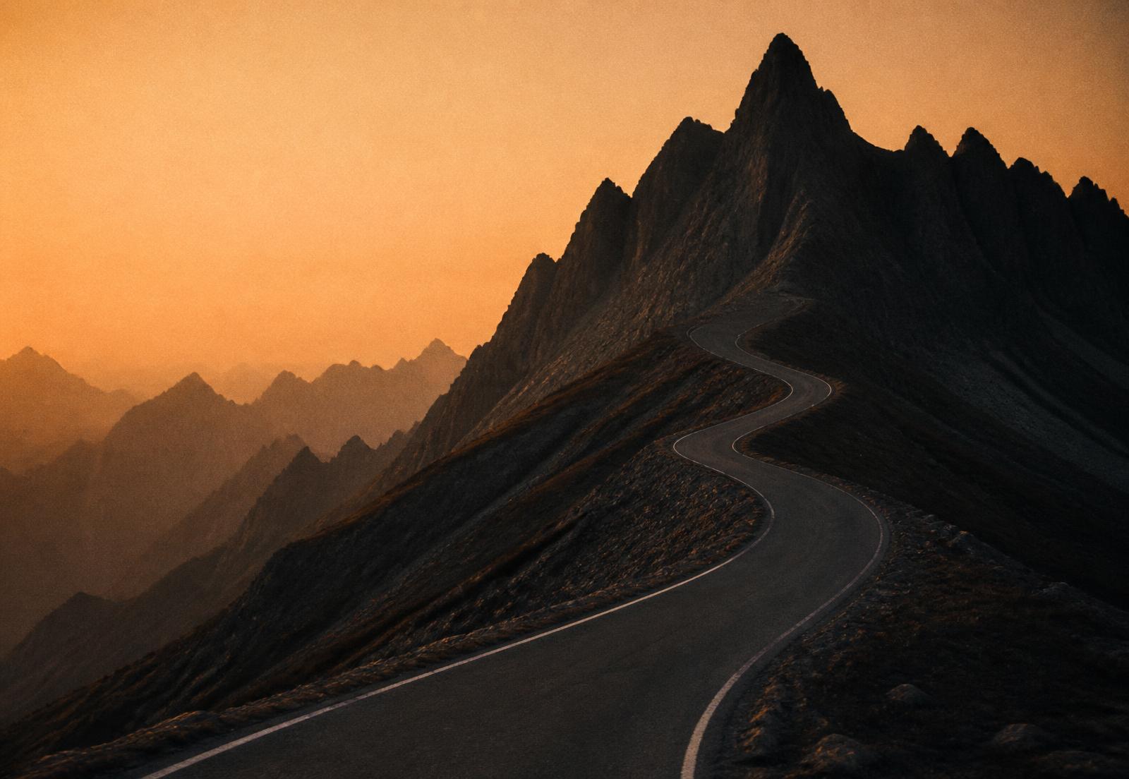 Empty mountain road climbing toward a dark ridge at dawn