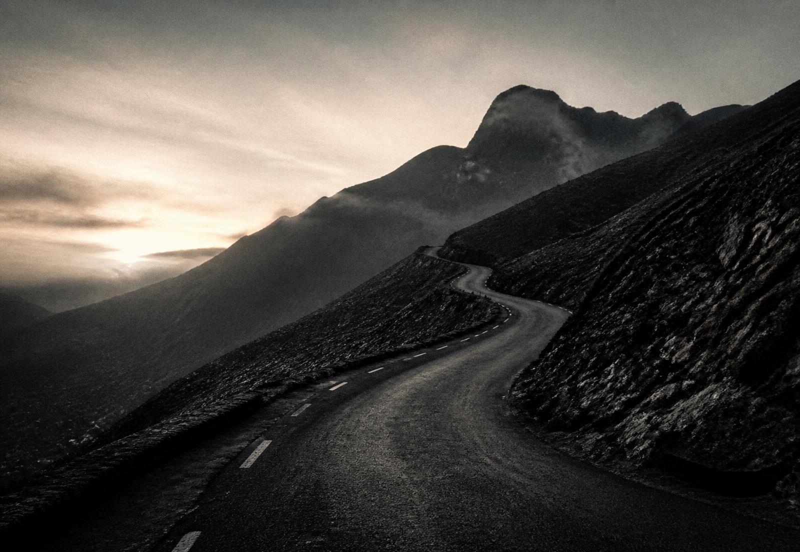 Empty mountain road climbing toward a dark ridge at dawn